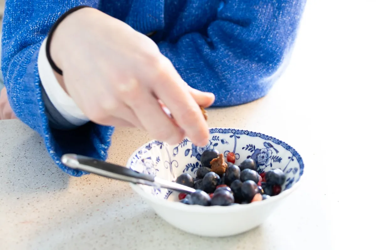 Arabella adding toppings to a patterned breakfast bowl filled with blueberries